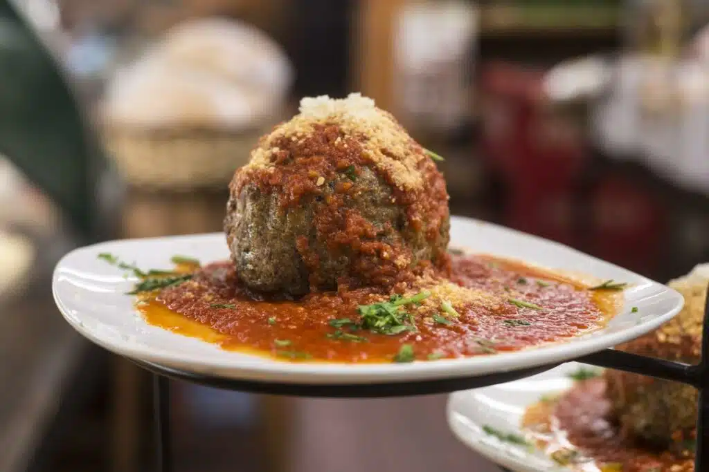 A giant one pound italian meatball covered in marinara sauce and parmesan cheese