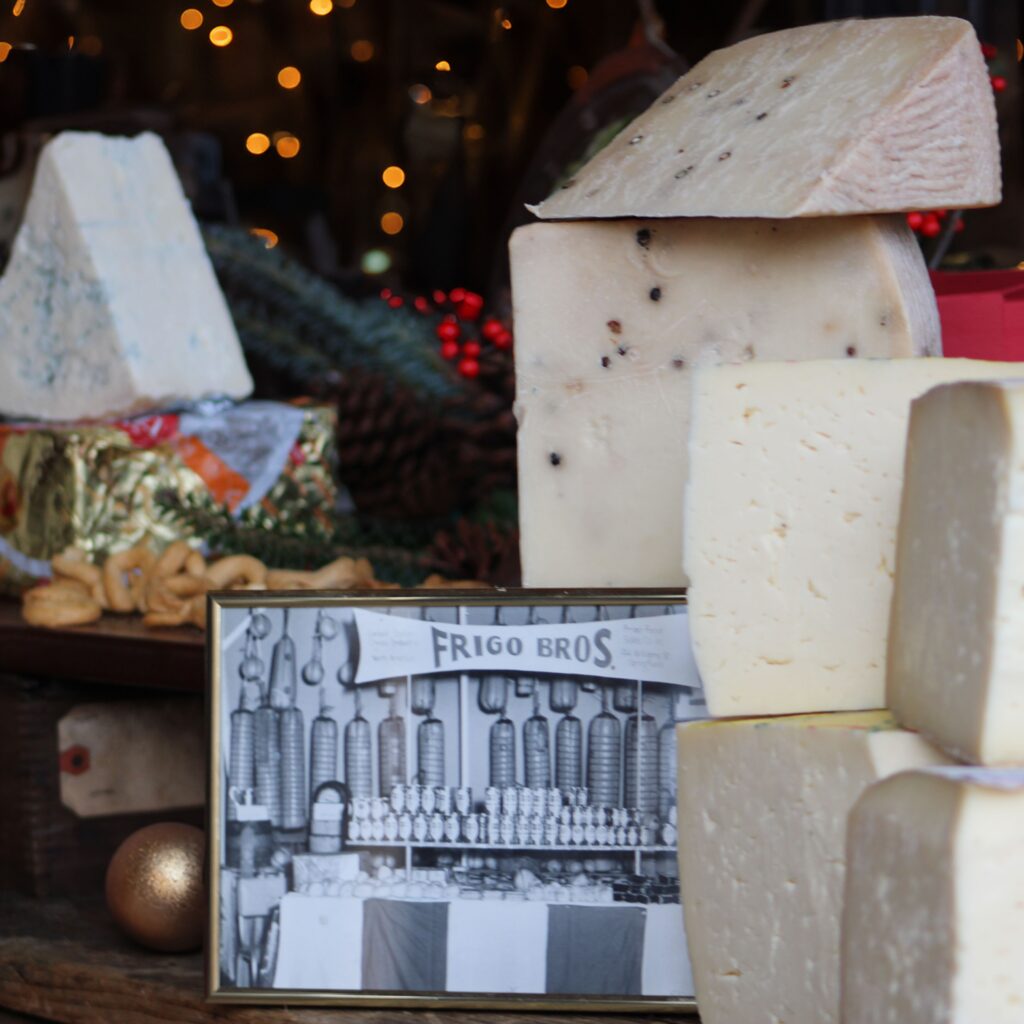 Old school photo of the frigo's deli with cheese hanging from the ceiling, next to fresh italian cheese.