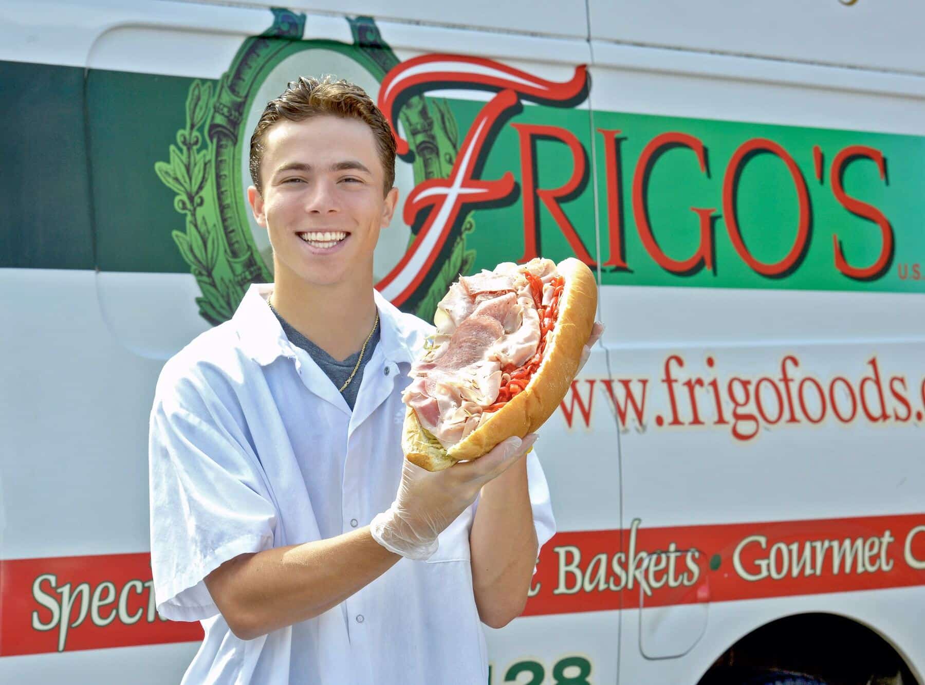 Frigo's team member holding a loaded Italian sub in front of the Frigo's van